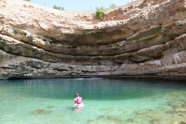 Ein Mädchen sitzt auf einem Schwimmreifen in einem türkisfarbenen Becken, umgeben von Felsen.