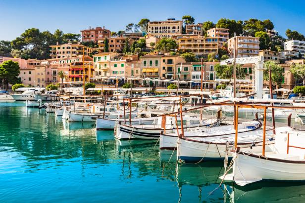 Boote liegen im Hafen von Port de Sóller vor der malerischen Stadtkulisse Mallorcas.