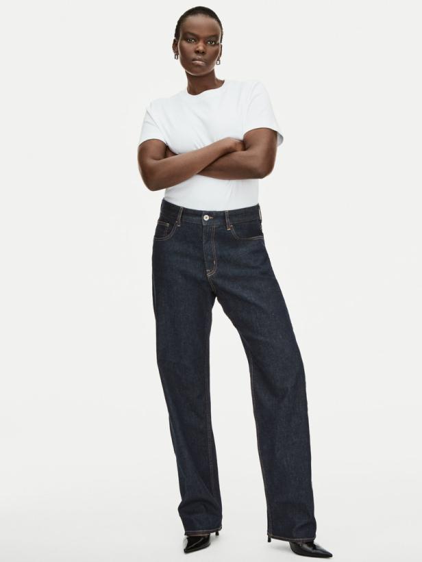 Eine Frau mit verschränkten Armen posiert in Jeans und einem weißen T-Shirt.