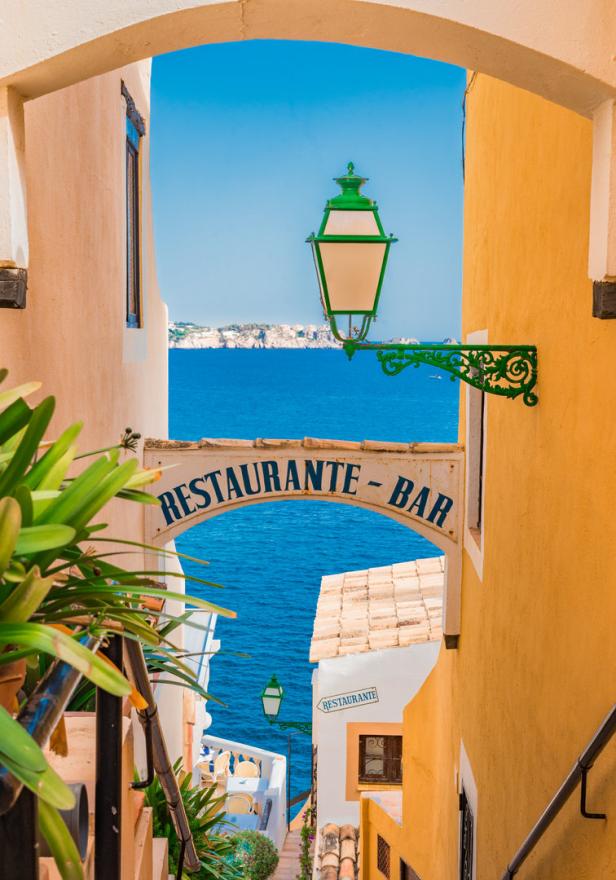 Ein Blick durch einen Torbogen auf das Meer und ein Restaurant-Bar-Schild.
