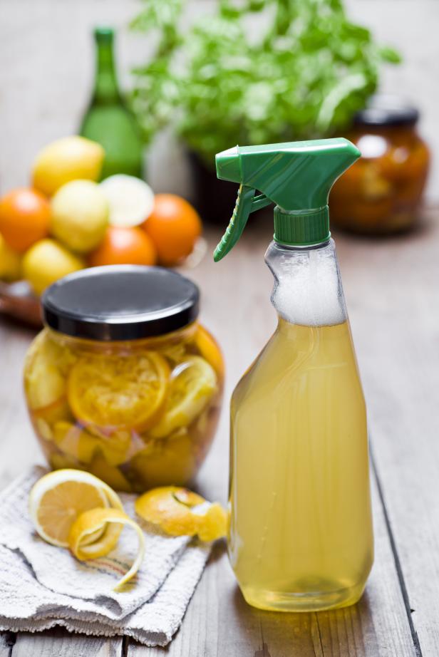 Eine Sprühflasche mit selbstgemachtem Reiniger steht neben Zitronen und Orangen.