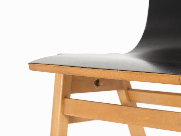 Detailansicht eines Holzstuhls mit schwarzer Sitzfläche.
