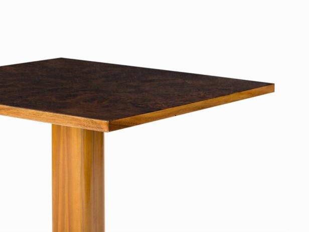 Detailansicht eines quadratischen Tisches mit dunkler Holzplatte und hellem Holzfuß.