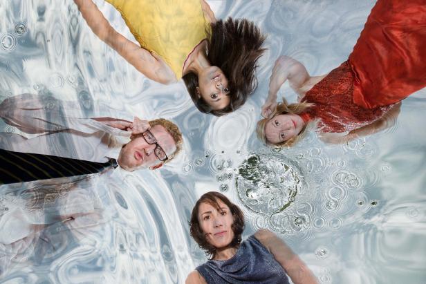 Vier Personen liegen unter einer Wasseroberfläche, die durch Regentropfen verzerrt ist.