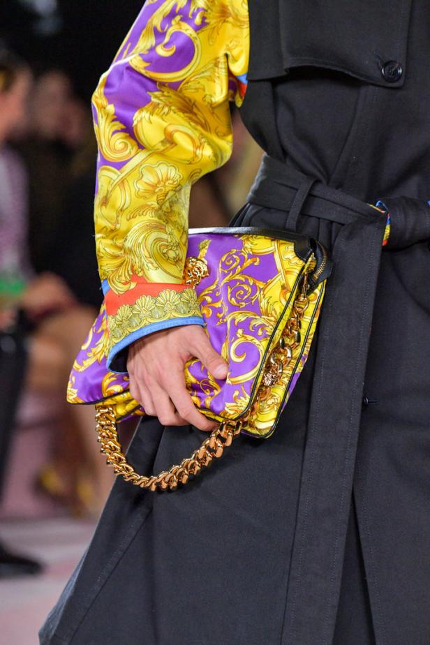 Ein Model präsentiert eine Handtasche mit goldenen Details und einem auffälligen Muster.