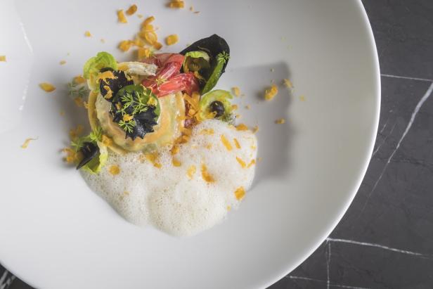 Ein Teller mit einem kunstvoll angerichteten Raviolo, garniert mit Gemüse und Schaum.