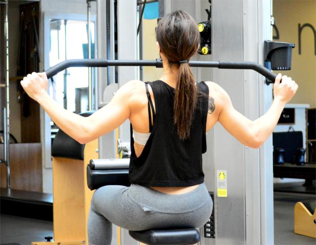 Eine Frau trainiert im Fitnessstudio an einer Latzugmaschine.