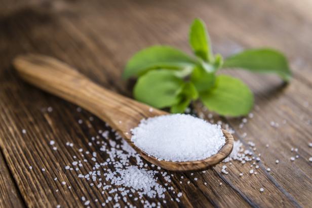 Ein Holzlöffel voller Stevia-Zucker liegt auf einem Holztisch.