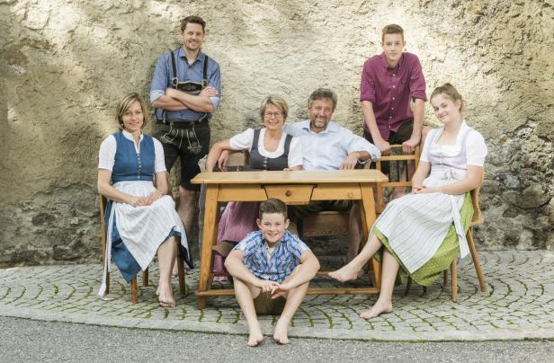 Eine Familie in Tracht posiert barfuß vor einer Mauer mit einem Holztisch.