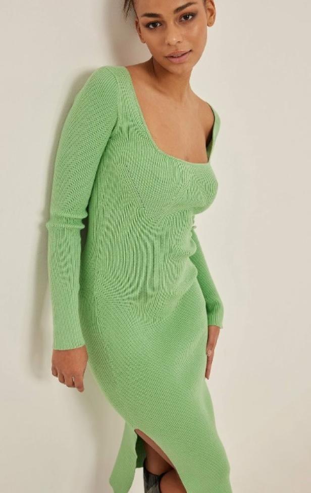 Eine Frau trägt ein hellgrünes, geripptes Strickkleid mit Schlitz.