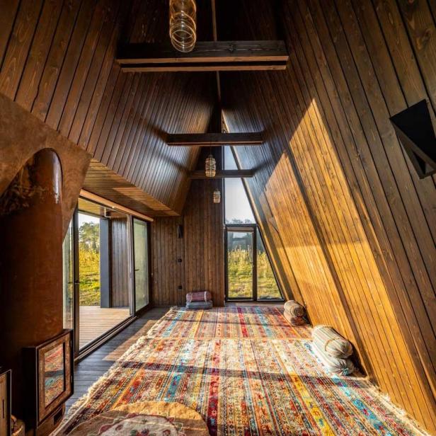Innenansicht eines Holzhauses mit einem bunten Teppich und Blick ins Grüne.
