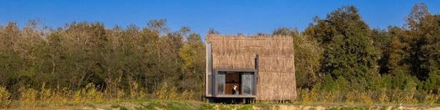 Ein kleines Haus mit Strohdach steht am Rande eines Waldes.