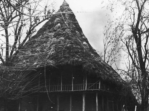 Ein traditionelles Haus mit einem kegelförmigen Strohdach steht auf Stelzen.