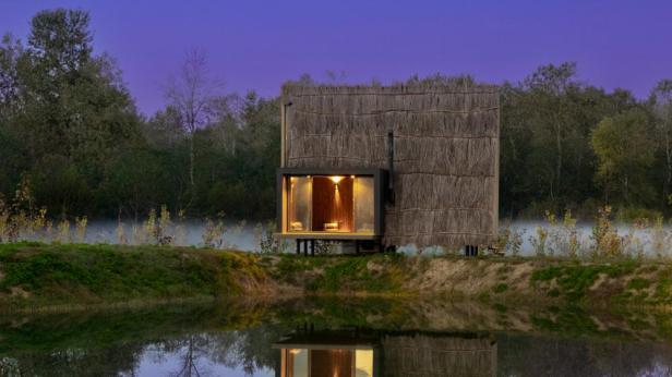 Ein kleines, strohgedecktes Haus steht am Ufer eines Sees.