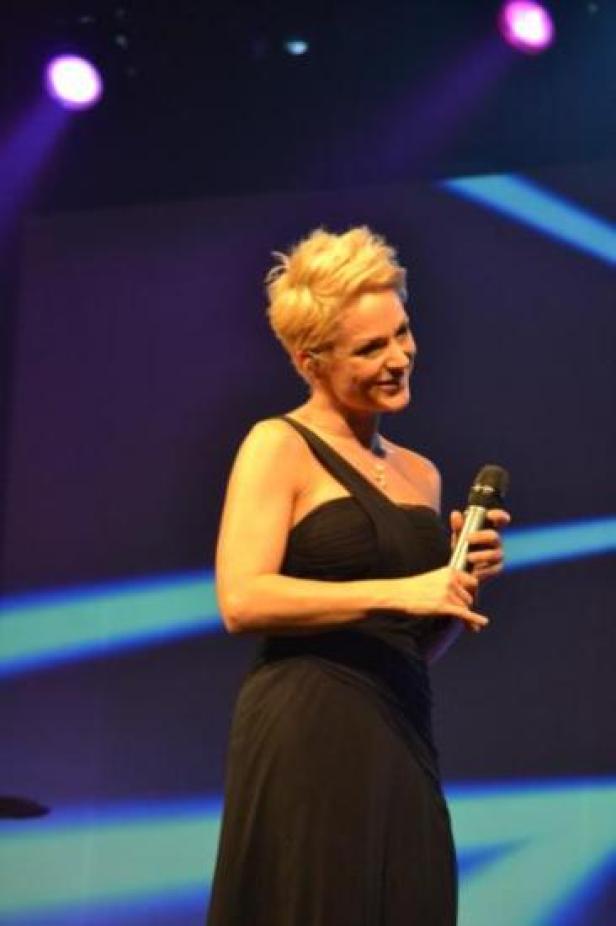 Eine Frau mit blonden, kurzen Haaren hält ein Mikrofon auf einer Bühne.