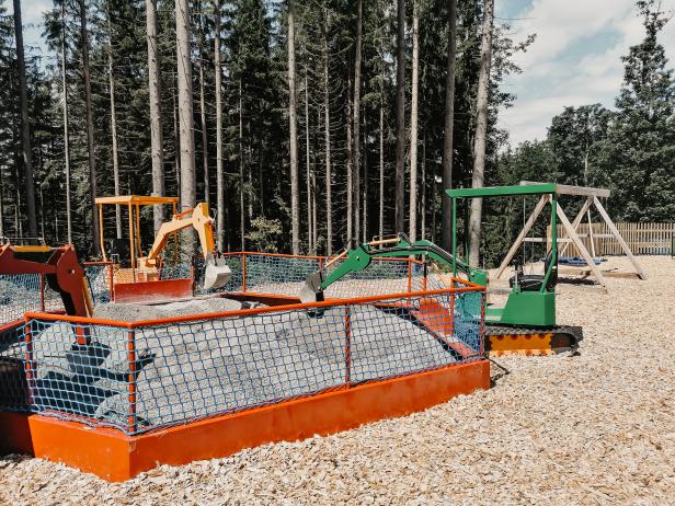 Ein Spielplatz mit Mini-Baggern und einem Sandkasten vor einem Wald.