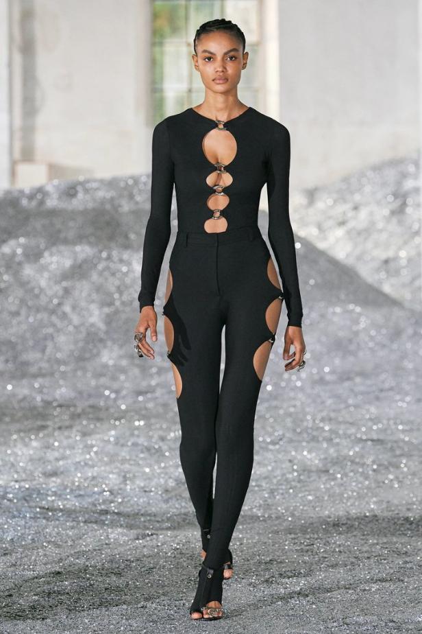 Eine Frau in einem schwarzen Outfit mit Cut-Outs posiert auf einem glitzernden Untergrund.
