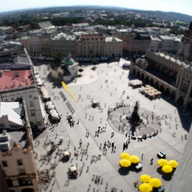 Ein Blick über den Marktplatz von Krakau mit vielen Menschen und gelben Sonnenschirmen.