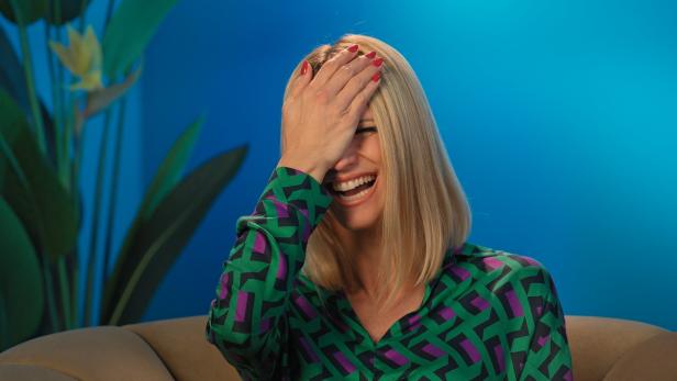 Eine lachende Frau mit blonden Haaren hält ihre Hand vor das Gesicht.