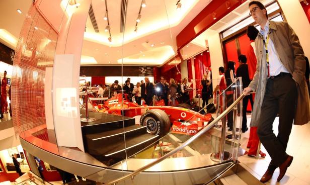 Ein roter Ferrari-Rennwagen steht in einem modernen Ausstellungsraum mit vielen Menschen.