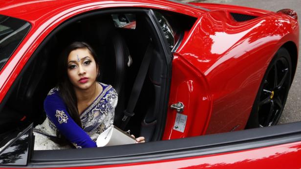 Eine Frau in traditioneller Kleidung sitzt in einem roten Ferrari.