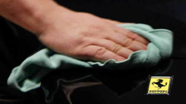 Eine Hand poliert einen schwarzen Ferrari mit einem Mikrofasertuch.