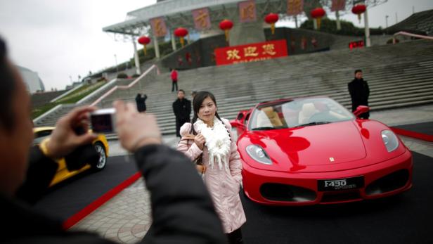 Eine Frau posiert vor einem roten Ferrari F430 Spider in China.