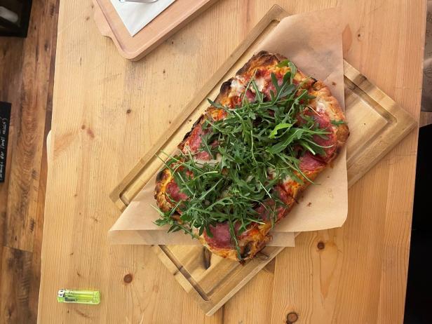 Eine rechteckige Pizza mit Rucola und Salami auf einem Holzbrett.