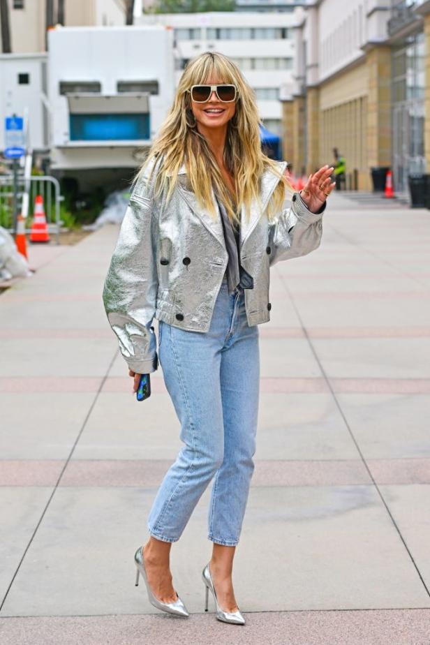 Heidi Klum trägt eine silberne Jacke, Jeans und silberne High Heels.