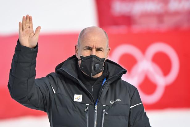 Ein Mann mit Maske winkt vor dem Hintergrund der Olympischen Ringe.
