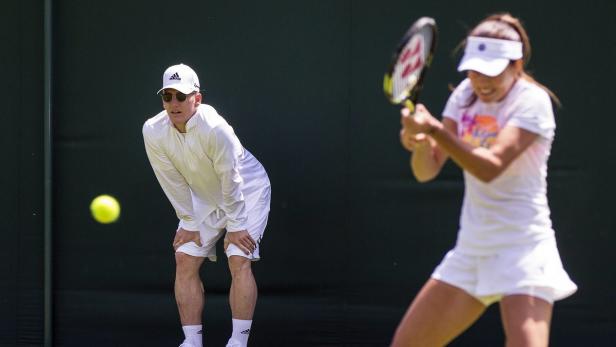 Eine Tennisspielerin schlägt einen Ball, während ein Trainer zusieht.