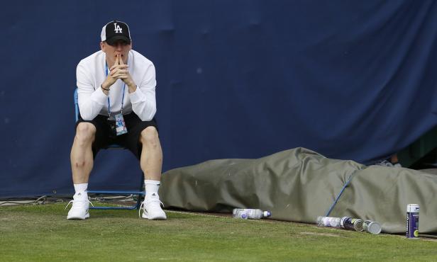 Ein Mann mit einer LA-Kappe sitzt nachdenklich auf einem Stuhl auf einem Tennisplatz.