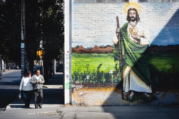 Ein Paar geht auf einem Bürgersteig an einem Wandgemälde von Jesus vorbei.