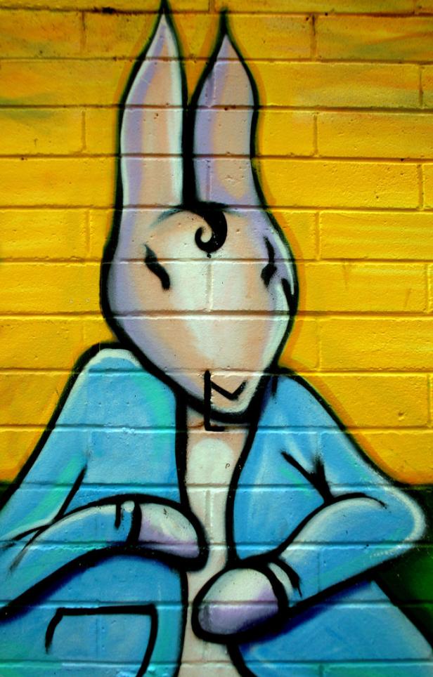 Graffiti-Kunstwerk eines anthropomorphen Hasen auf einer gelben Backsteinmauer.
