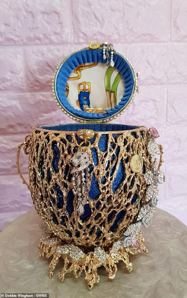 Ein goldenes Schmuckkästchen in Form eines Fabergé-Eies mit blauem Innenfutter und diversen Schmuckanhängern.