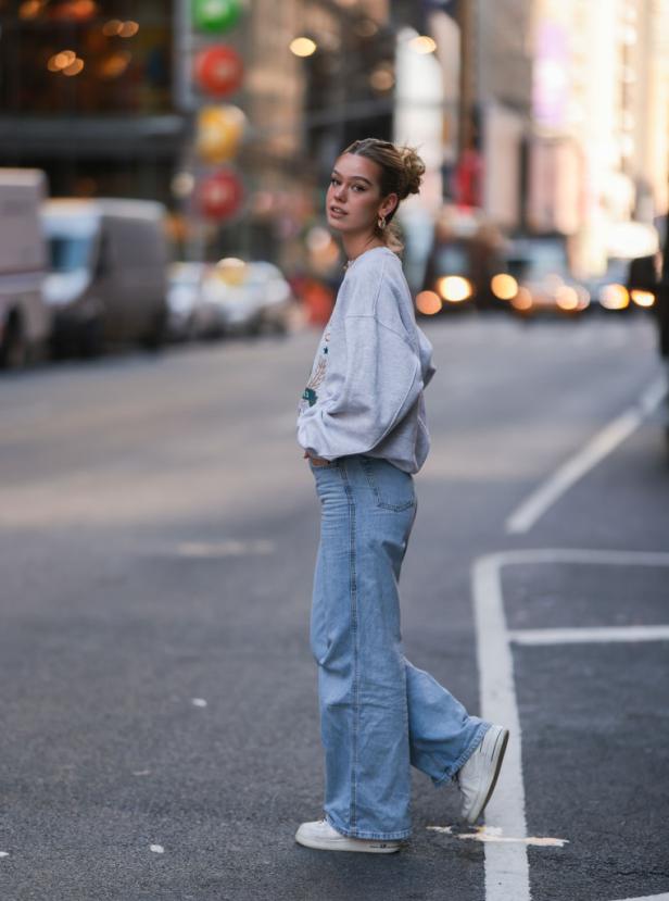 Eine junge Frau in Jeans und einem Sweatshirt überquert eine Straße in der Stadt.