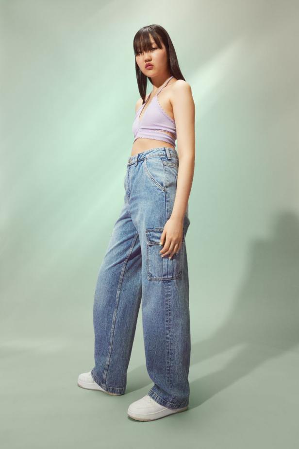 Eine junge Frau posiert in einem lila Top und weiten Jeans mit Cargotaschen.