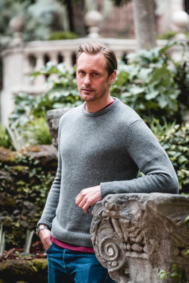 Alexander Skarsgård posiert lässig an einer steinernen Balustrade.