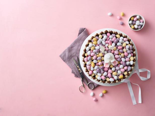 Ein Osternest-Kuchen mit Schokoladeneiern und einem Zuckerhasen auf einem rosa Hintergrund.