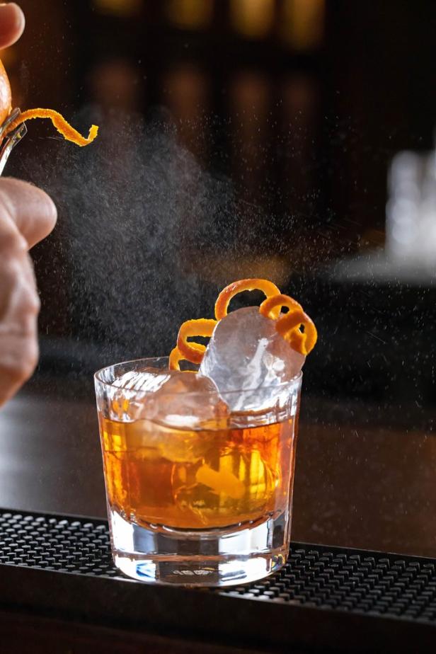 Ein Cocktail wird mit Orangenzesten und einem Spritzer verfeinert.