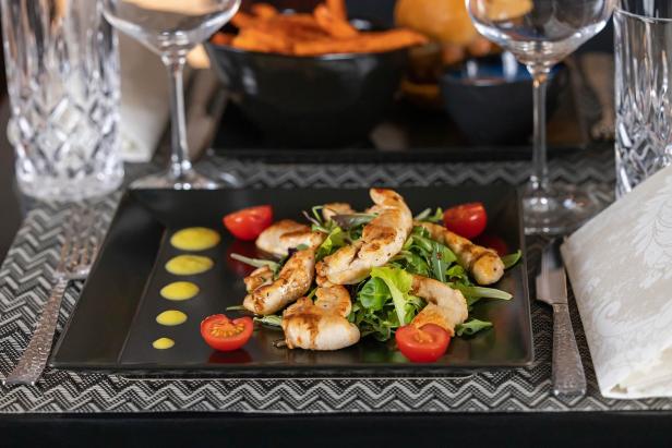 Ein Teller mit Hähnchenstreifen, Salat und Tomaten auf einem gedeckten Tisch.