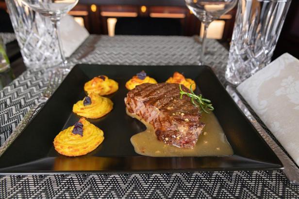 Ein Steak mit Kartoffelpüree und Soße auf einem schwarzen Teller.