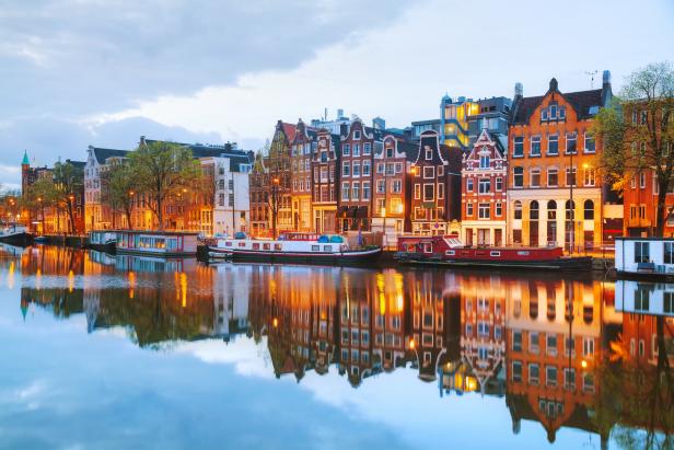 Kanal in Amsterdam mit Hausbooten und beleuchteten Häusern am Ufer.