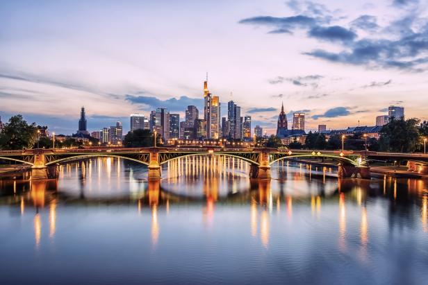Die Skyline von Frankfurt am Main bei Dämmerung, gesehen von einer Brücke über den Main.
