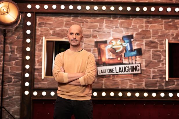 Ein Mann steht vor einer Wand mit dem „Last One Laughing“-Logo.