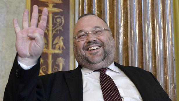 Ein lachender Mann mit Brille zeigt vier Finger.