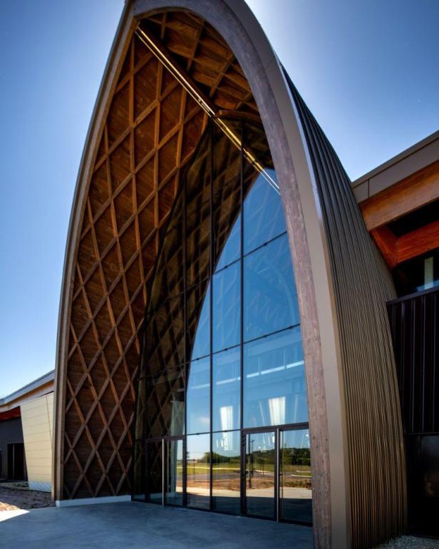 Die Fassade eines modernen Gebäudes mit einem großen Glasbogen und Holzdetails.