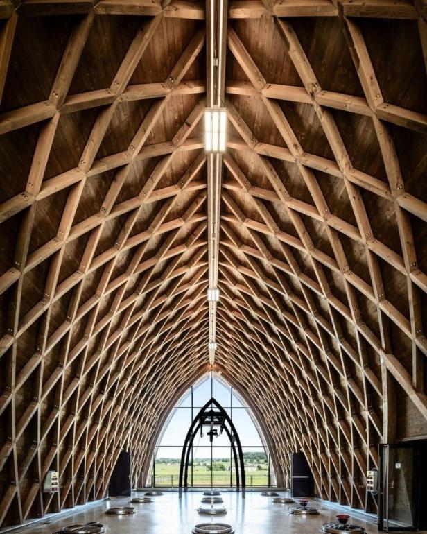 Das Innere einer modernen Kapelle mit einem hölzernen Gitterdach und einem Blick auf die Landschaft.