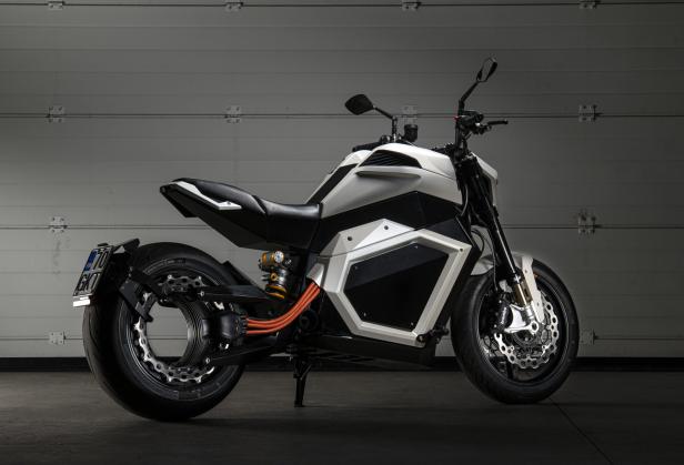 Ein weißes und schwarzes Elektromotorrad steht vor einer grauen Garagenwand.