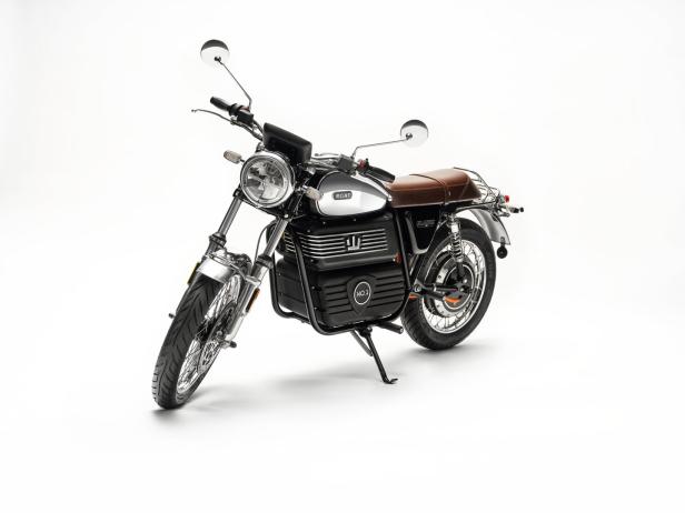 Ein silbernes Elektromotorrad mit braunem Ledersattel steht auf einem weißen Hintergrund.